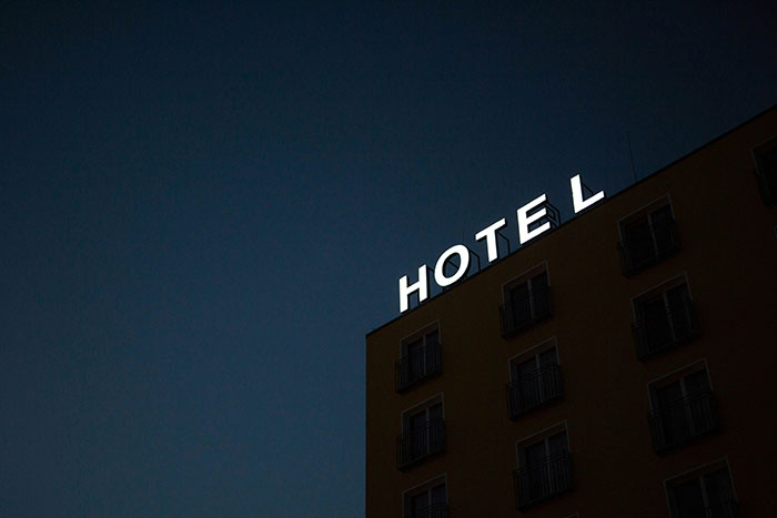 Hotel building at night with glowing sign, representing unspoken hospitality rules.