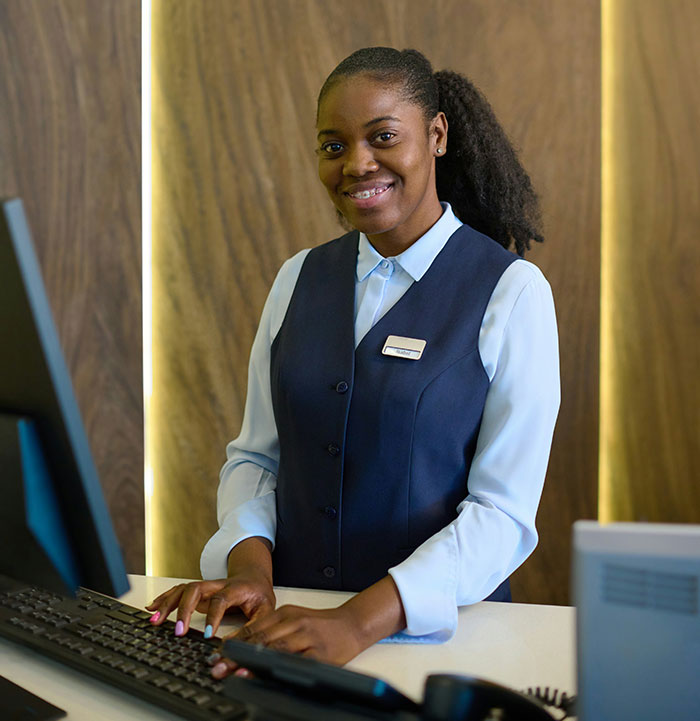 Hotel staff at reception desk, wearing a blue uniform, embodying unspoken hospitality rules.