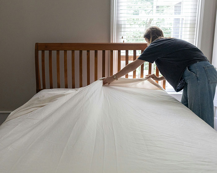 Person making a bed in a hotel room, showcasing common etiquette in hospitality.