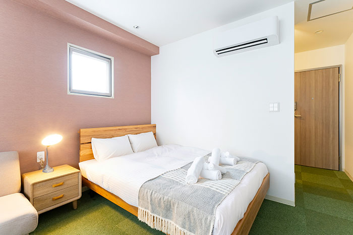 Hotel room with neatly arranged bed, soft lighting, and rolled towels on a light-colored blanket.