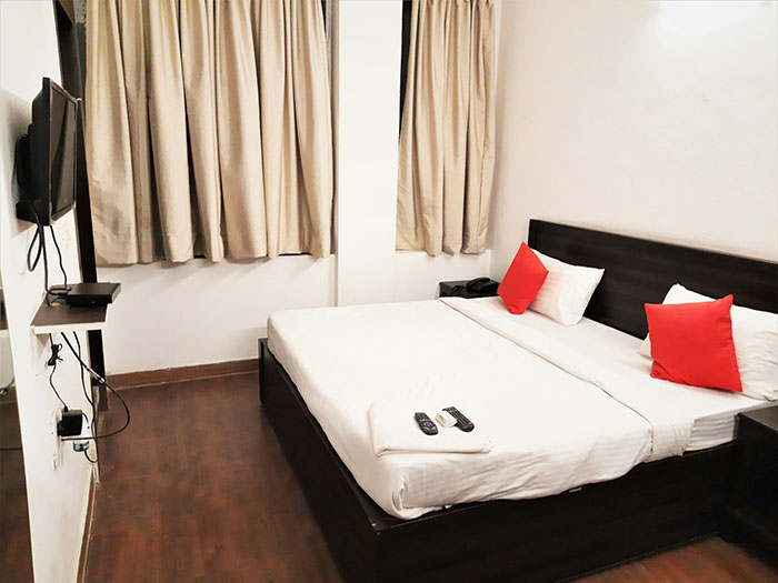 Stylish hotel room with double bed, red cushions, TV, and curtains, illustrating hotel etiquette familiarity.