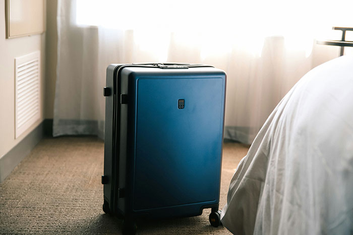 Blue suitcase on a hotel room floor next to a bed, symbolizing travel etiquette.