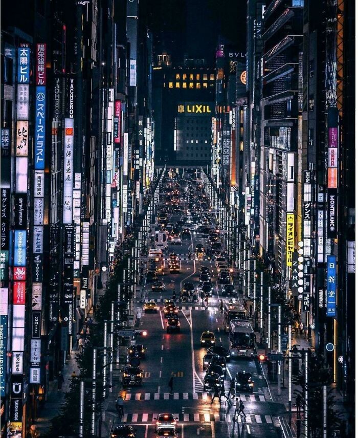 Urban hell: Nighttime view of a bustling city street filled with cars and illuminated skyscrapers.