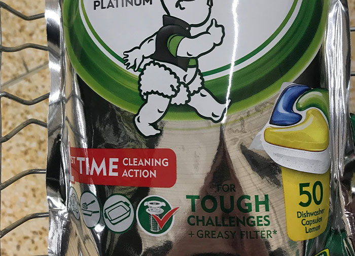 Dishwasher tablets package with baby holding gun illustration, indicating using things wrong way.