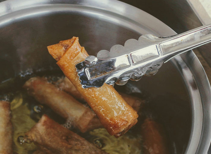 Tongs holding fried spring roll, illustrating using things the wrong way.