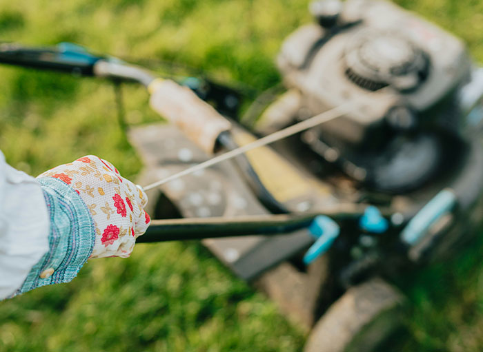 Person starting a lawnmower incorrectly, highlighting using things the wrong way.