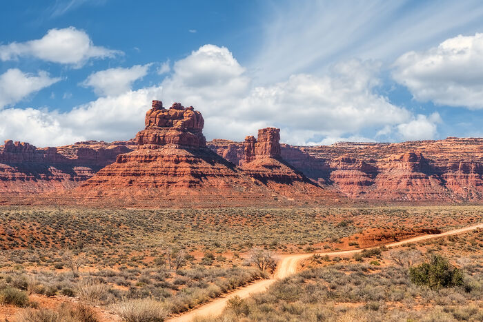 Red rock formations under a blue sky in a desert landscape, tallest near the horizon.