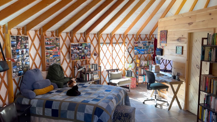 Interior of a self-built yurt with bed, desk, and bookshelves, showcasing off-grid lifestyle details.