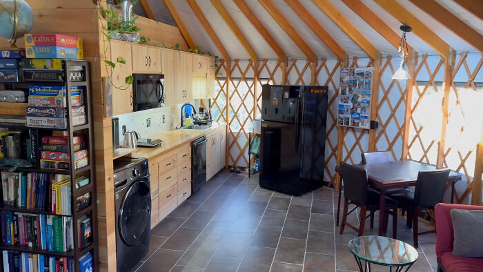 Interior of a self-built off-grid yurt featuring a kitchen, dining area, and bookshelf filled with games and books.