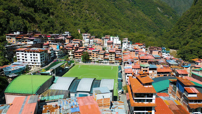 Aerial view of colorful buildings and a soccer field in a lush mountainous region of Tuscany, Italy.