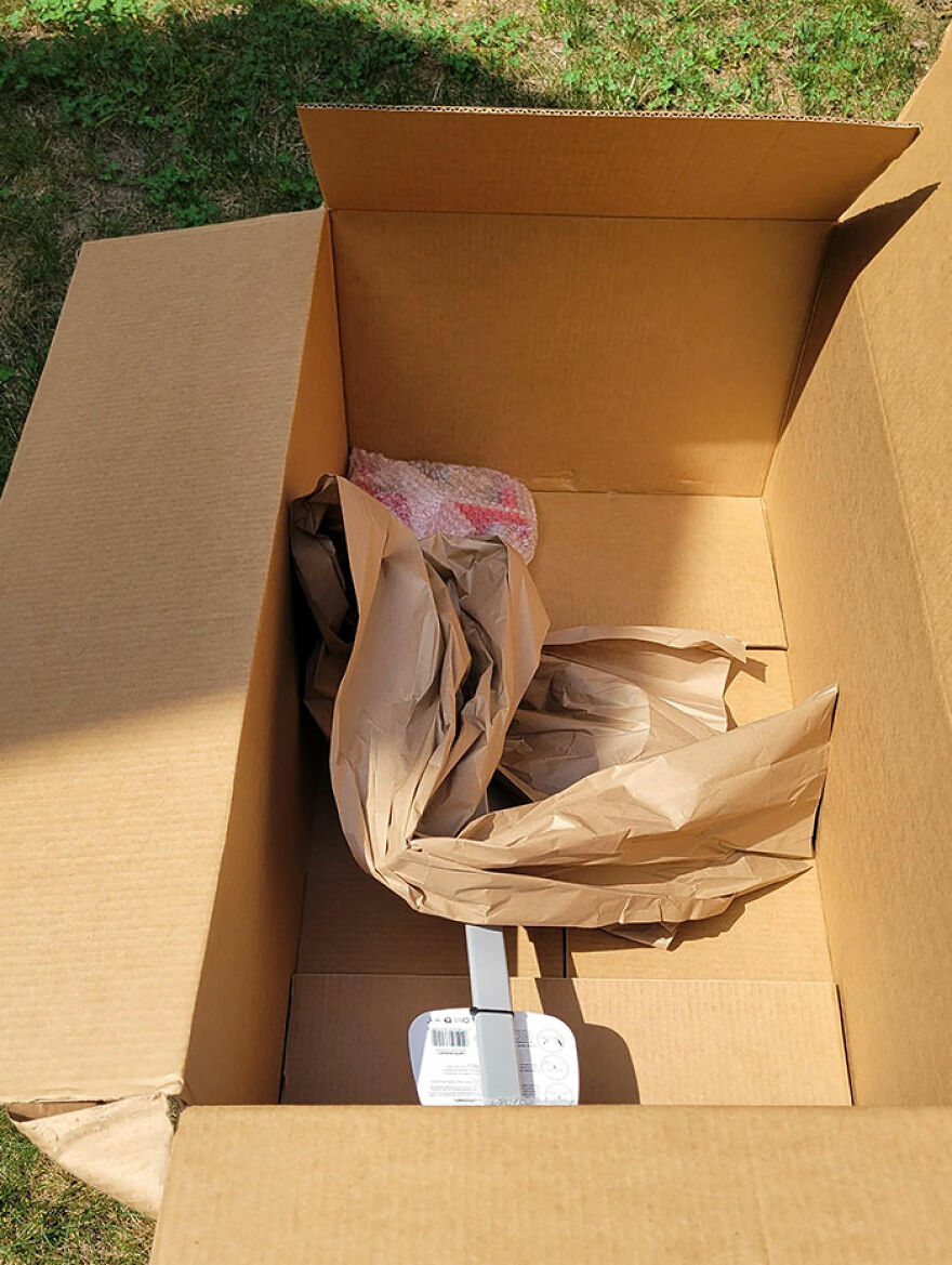 Large cardboard box with wasteful, unnecessary packaging materials inside on a grassy background.