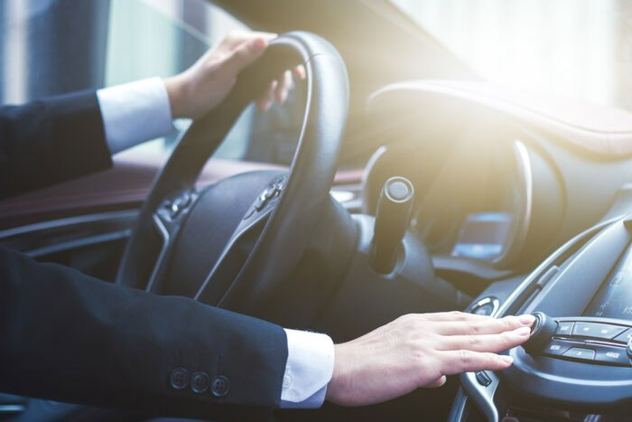 "Bodyguard driving luxury car, adjusting radio, sunlight streaming through windshield."