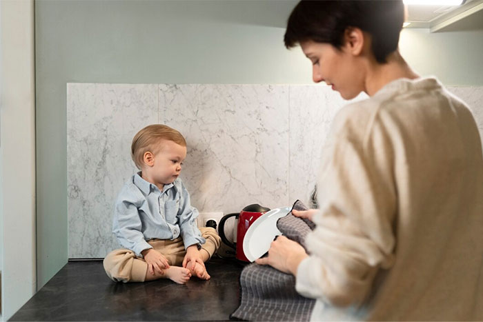 Parent folding clothes in kitchen while child sits nearby.