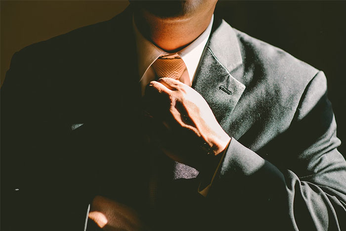 Man adjusting tie, wearing a suit, representing work life of bodyguards for the wealthy.