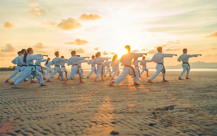 Group practicing martial arts on the beach, training for roles as bodyguards for the wealthy at sunset.