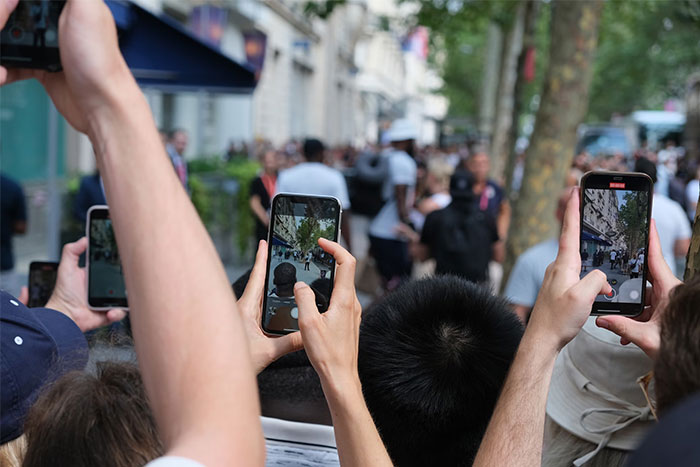 Crowd taking photos with phones, capturing a busy street scene, relevant to bodyguard experiences for the wealthy.