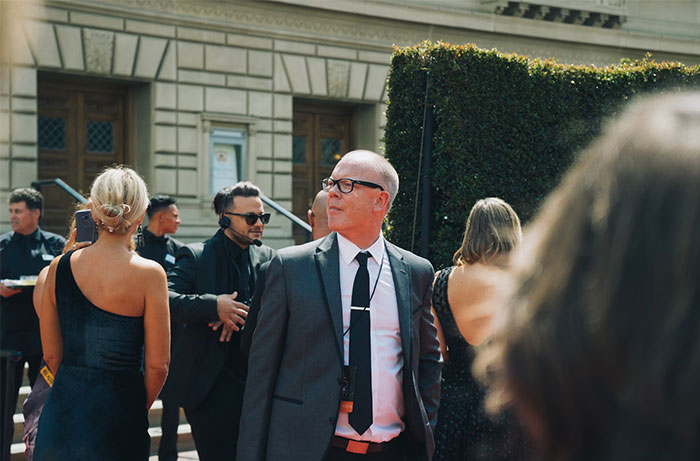 Bodyguard in a suit and tie looks attentive at upscale outdoor event, ensuring safety for the wealthy attendees.