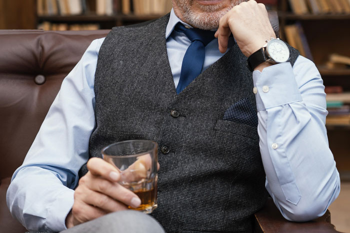 Man in a vest and tie, sitting with a drink, possibly a wealthy client of a bodyguard, showcasing luxury lifestyle.