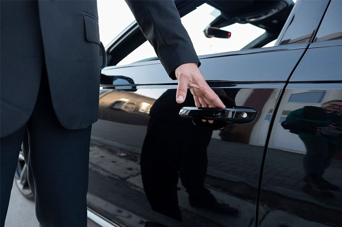 A bodyguard in a suit opens the door of a luxury car for a client, showcasing the role of working for the wealthy.