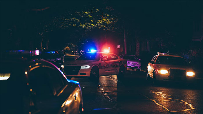 Police cars with flashing lights in a dark area, related to work as a bodyguard for the wealthy.