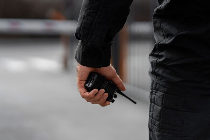 Bodyguard holding a walkie-talkie, dressed in black, ready for security duty.