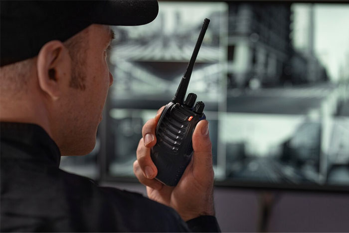 Bodyguard communicating via radio, monitoring security screens in a control room.