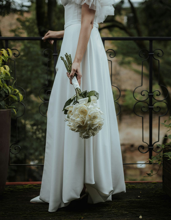 Bride holding bouquet, standing on balcony, evokes wedding day emotions and reflections.