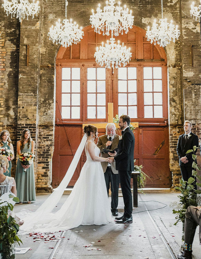 Bride and groom exchanging vows in a rustic venue, elegant chandeliers overhead, symbolizing a pivotal wedding moment.