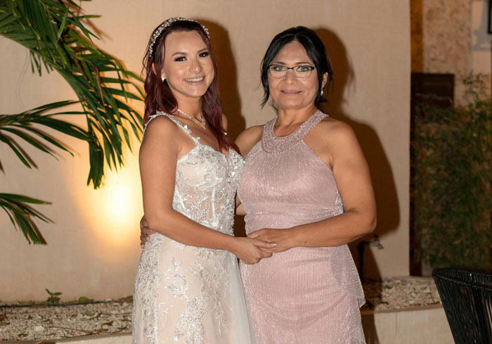 Stepmom in a pink dress stands with the bride at the wedding, next to greenery.