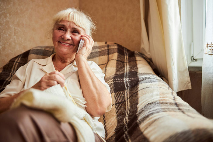 Smiling stepmom knitting on a plaid sofa, dressed in a white shirt.