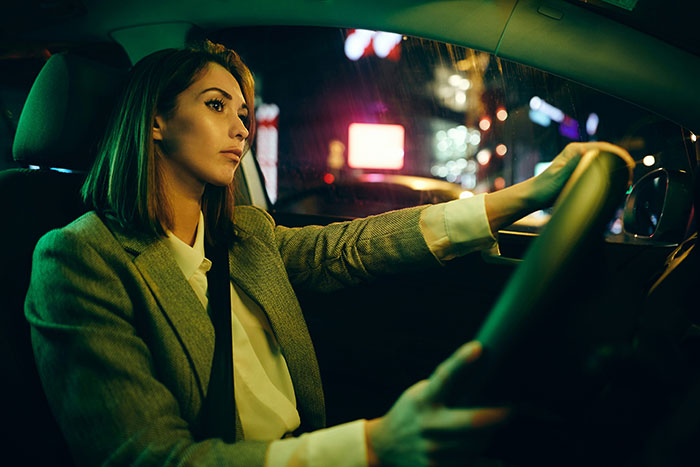 A driver listens intently while driving at night, city lights visible through the car window.