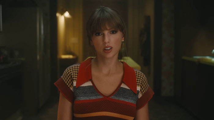 A woman with bangs in a colorful striped top, sitting in a dimly lit room, related to stories about rich people.