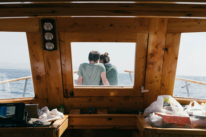 Two people sitting on a boat, viewed through a cabin window, enjoying a scenic ride, evoking stories of rich people.