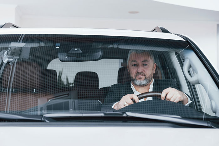 Man driving a luxury car, looking focused, symbolizing the experience of hearing stories about wealthy individuals.