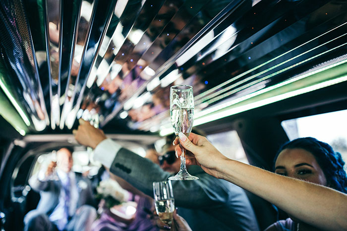 Guests in a limousine raising champagne glasses, celebrating, reflecting on stories about rich people.