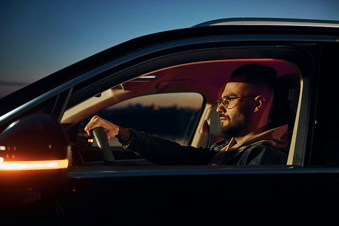 Driver in a car at sunset, experiencing stories about rich people while driving.