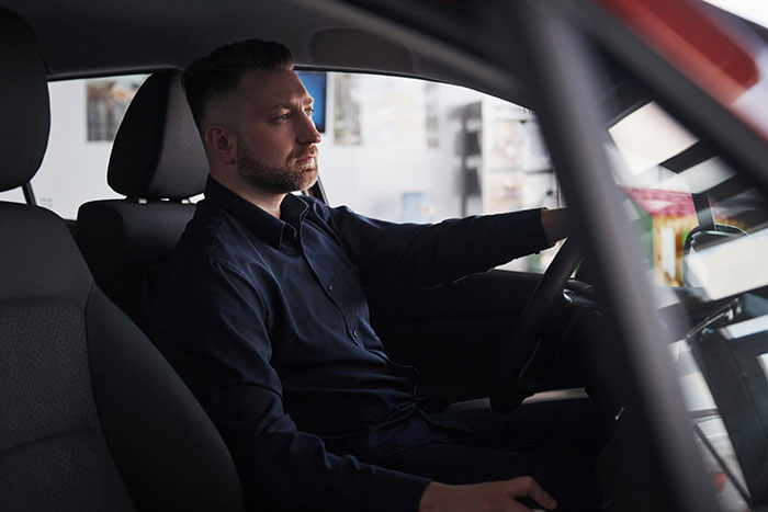 Driver in a car, focused and thoughtful, as he hears stories about rich people.