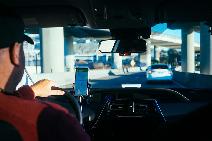 Driver in a car on the highway, smartphone with a map app mounted on the dashboard, rich people stories in mind.