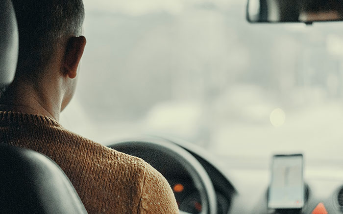 Driver in a car, focused on the road, possibly hearing stories about rich people while working.