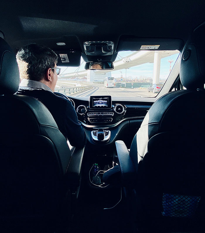 "Driver with sunglasses in a car, possibly listening to rich people's stories while on the road."