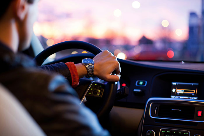 Driver in a car with sunset view, hearing gossip about wealthy passengers.