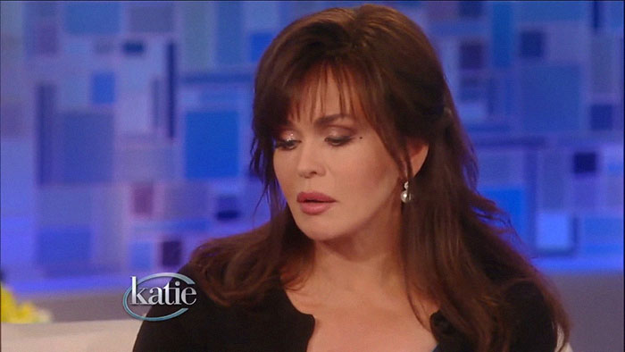 A woman with long brown hair, wearing earrings, in a studio setting, related to rich people stories from drivers.