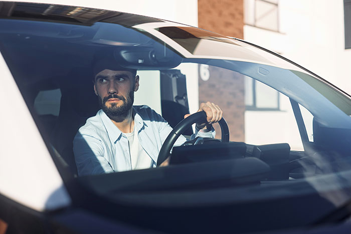 Driver in a car, looking thoughtful, with hands on the steering wheel, hearing stories about rich people.