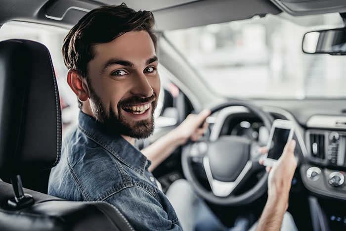 Smiling driver holding a phone, possibly sharing stories about rich people while behind the wheel.