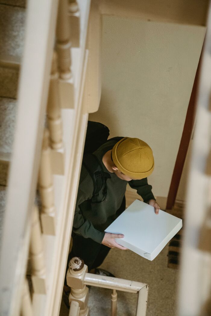 "Delivery person in a yellow hat carrying a package up the staircase, highlighting awkward delivery scenarios."