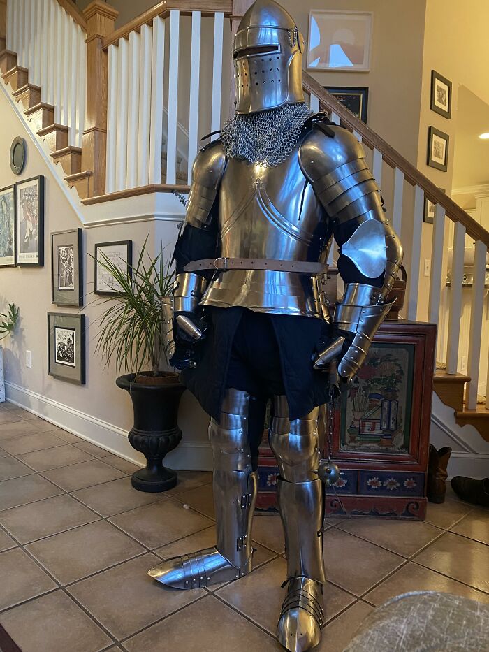 A person in a full suit of medieval armor stands awkwardly indoors, embodying an unhinged delivery moment.