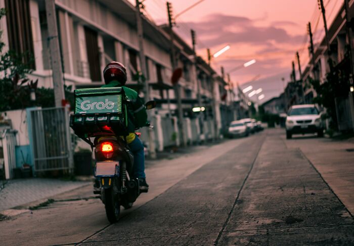 Delivery rider on a motorbike at sunset, carrying a Grab backpack on an urban street.