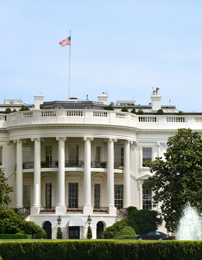 White House with flag flying on top, showcasing classic architecture and vibrant greenery.