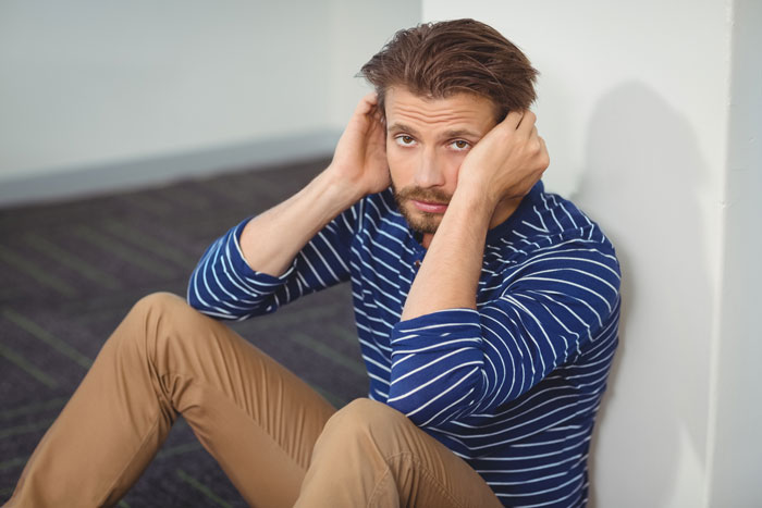 Man sitting on floor in a striped shirt, looking frustrated, related to fixing family attitude issues.