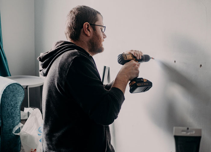 Man using a drill on a wall; showcasing DIY skills but frustrated with in-laws.